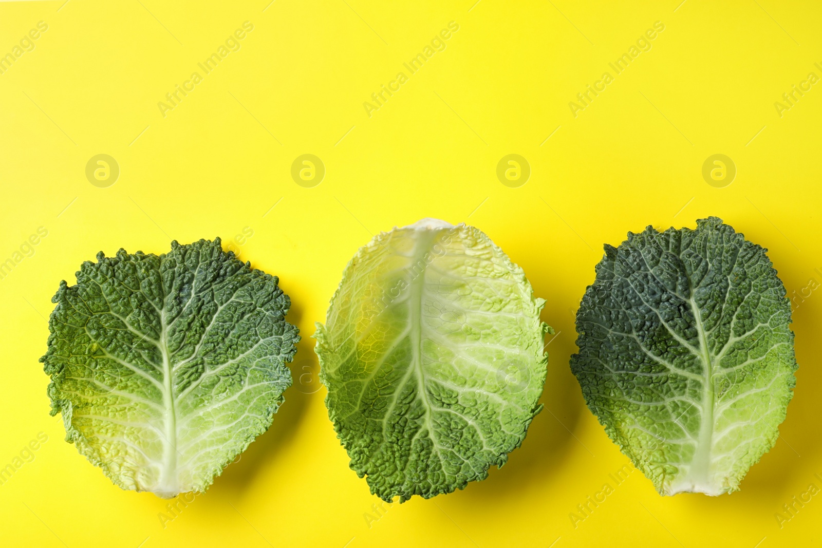 Photo of Fresh savoy cabbage leaves on yellow background, flat lay