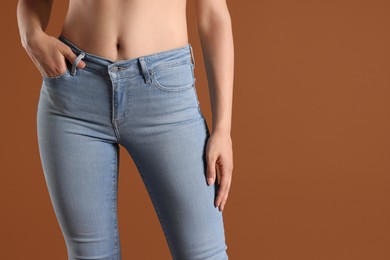 Woman wearing stylish light blue jeans on brown background, closeup. Space for text