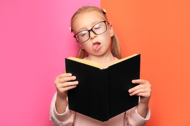 Cute little girl in glasses with book on colorful background