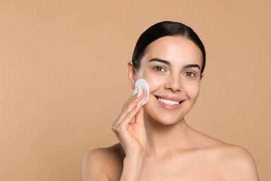 Photo of Young woman using cotton pad with micellar water on beige background, space for text