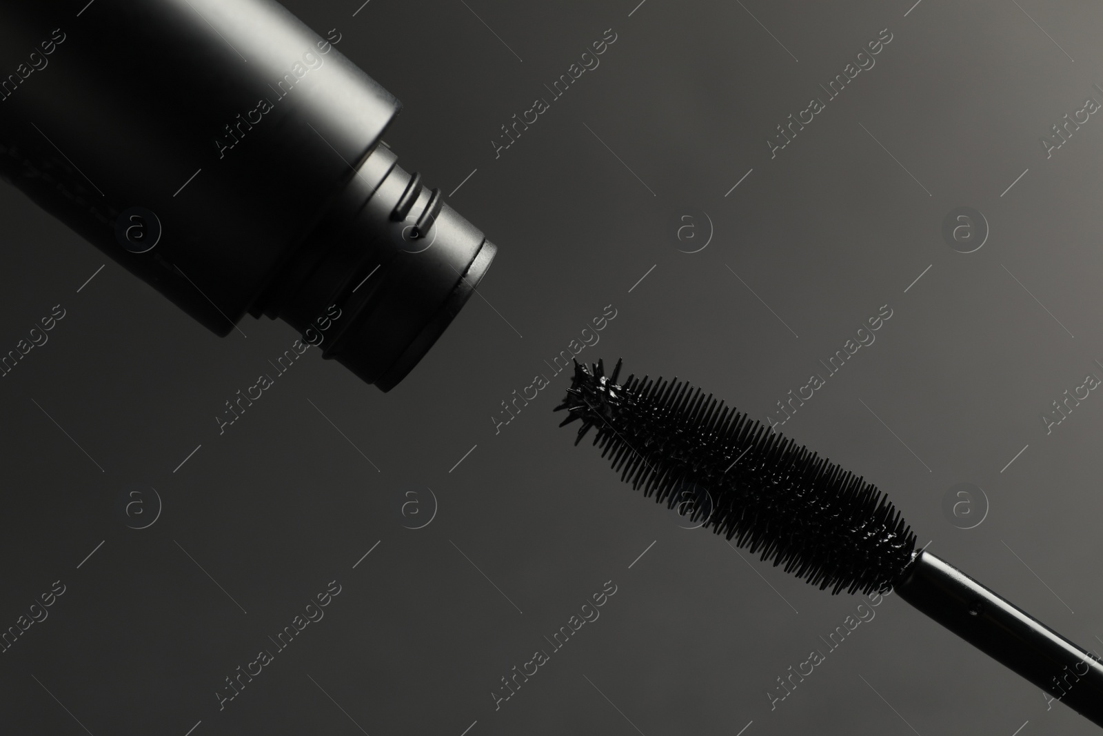 Photo of Black mascara with wand on grey background, closeup