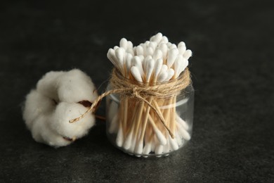 Photo of Cotton swabs and flower on black table, closeup. Space for text