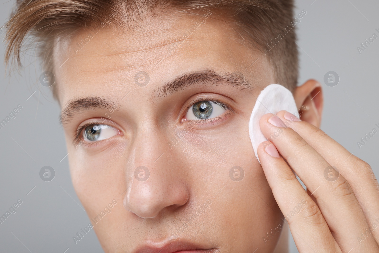 Photo of Man cleaning face with cotton pad on grey background, closeup