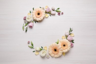 Wreath made of beautiful flowers and green leaves on white wooden background, flat lay. Space for text