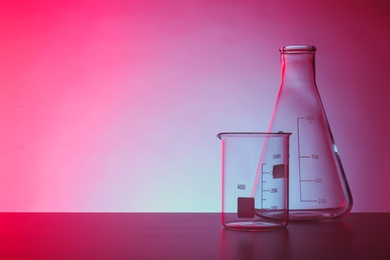 Empty chemistry laboratory glassware on table against color background