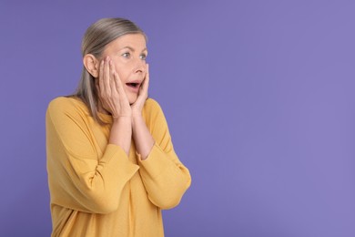 Portrait of surprised senior woman on violet background, space for text