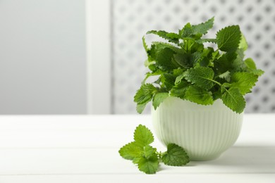 Photo of Fresh lemon balm in bowl on white wooden table, space for text