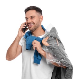 Man holding garment cover with clothes while talking on phone, isolated on white. Dry-cleaning service