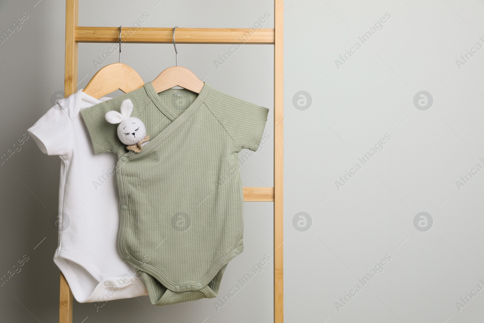 Photo of Baby bodysuits hanging on ladder near light wall, space for text