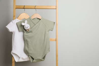 Photo of Baby bodysuits hanging on ladder near light wall, space for text