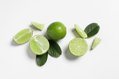 Fresh ripe limes and leaves on white background, flat lay