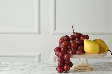 Photo of Dessert stand with fresh ripe pears and grapes on white marble table, space for text