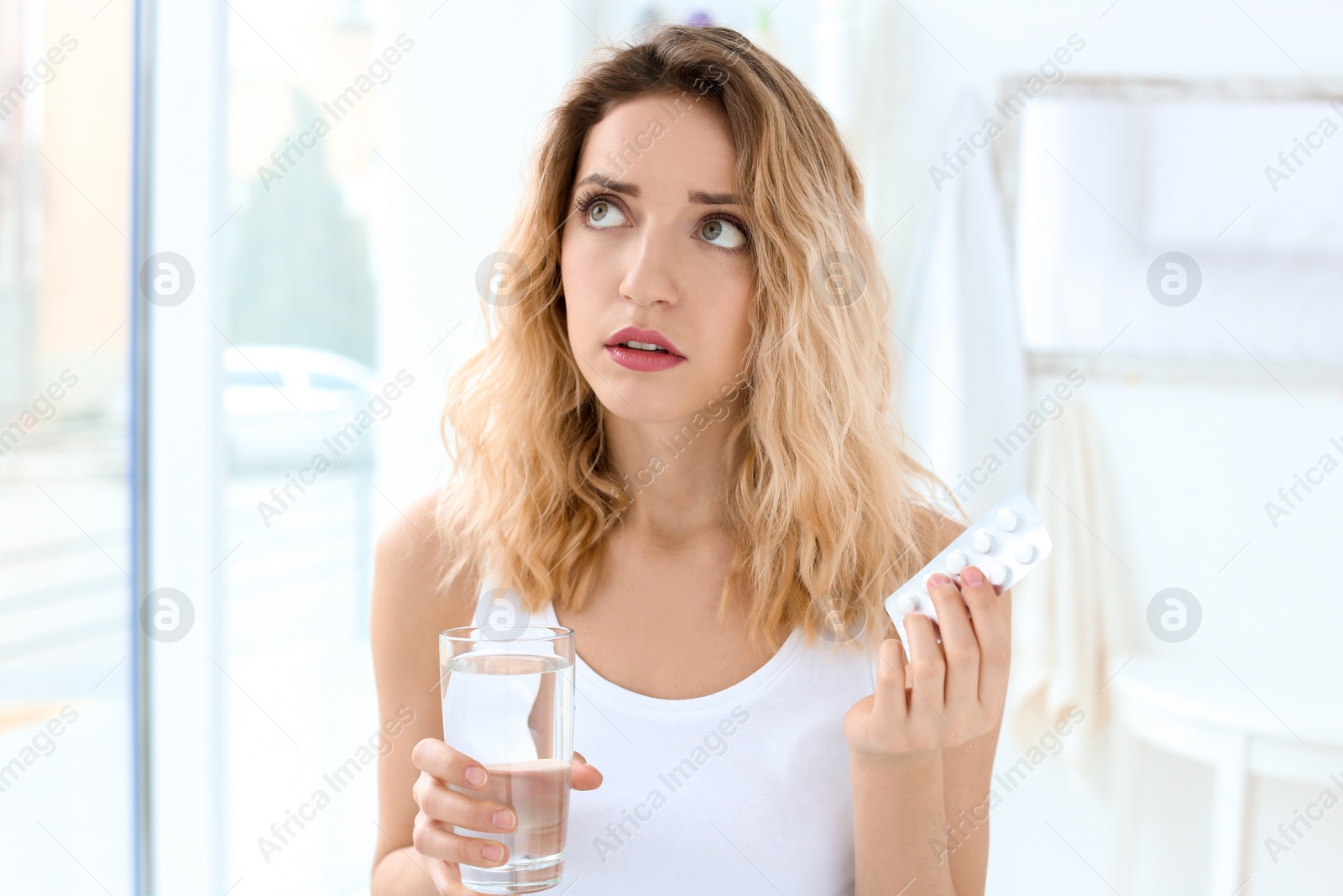 Photo of Young woman with pills and glass of water indoors