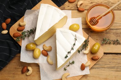 Tasty Camembert cheese with thyme, honey and nuts on wooden table, flat lay