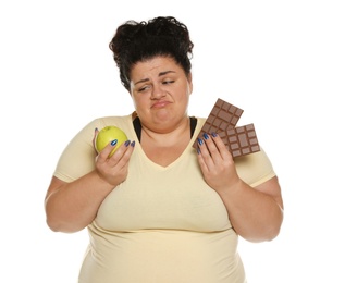 Emotional overweight woman with apple and chocolate on white background