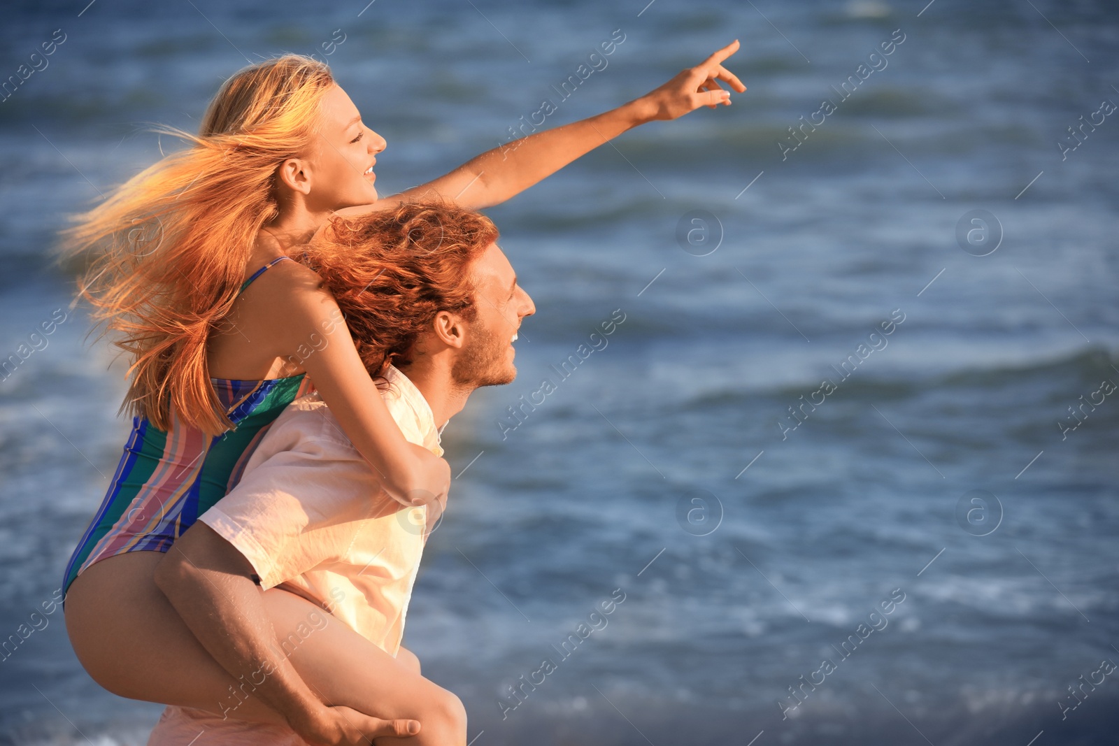 Photo of Young woman in bikini and her boyfriend having fun on beach at sunset. Lovely couple