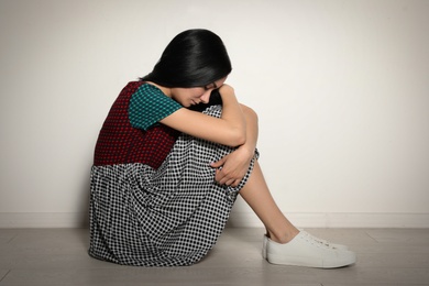 Photo of Upset young woman sitting on floor near light wall