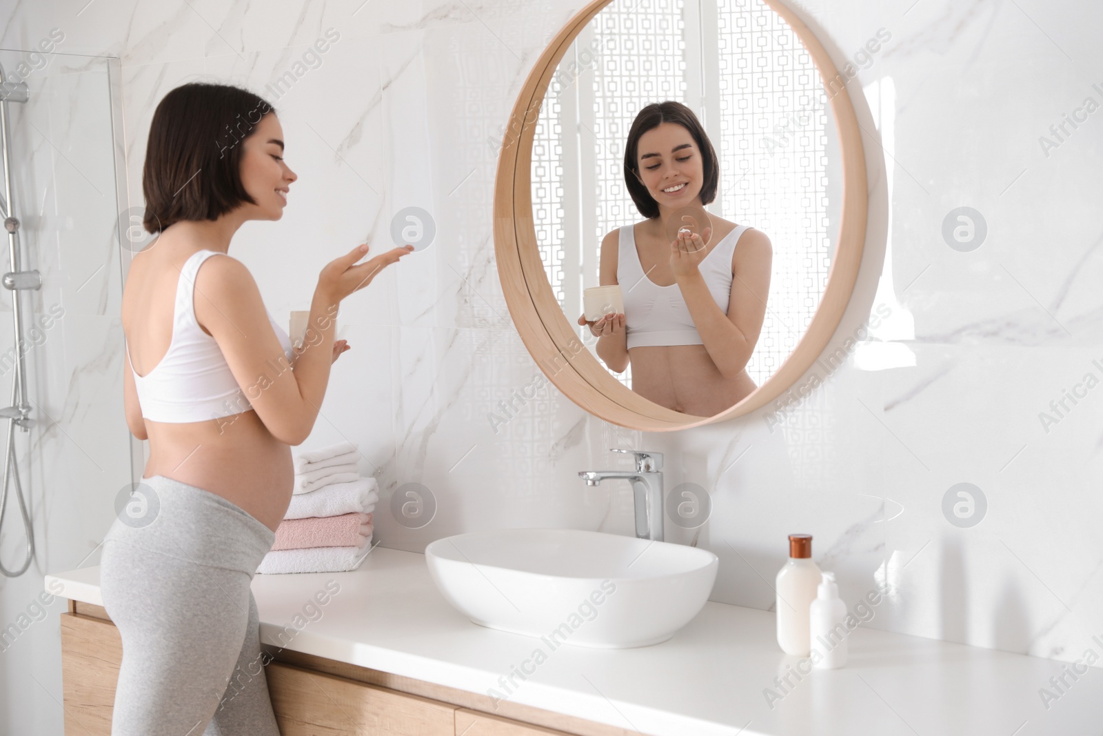 Photo of Young pregnant woman with cosmetic product in bathroom