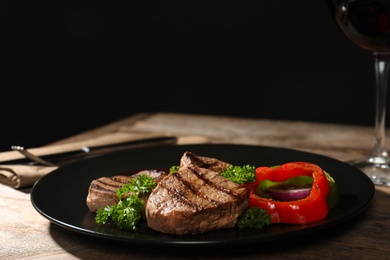 Photo of Plate with grilled meat and garnish on table against black background