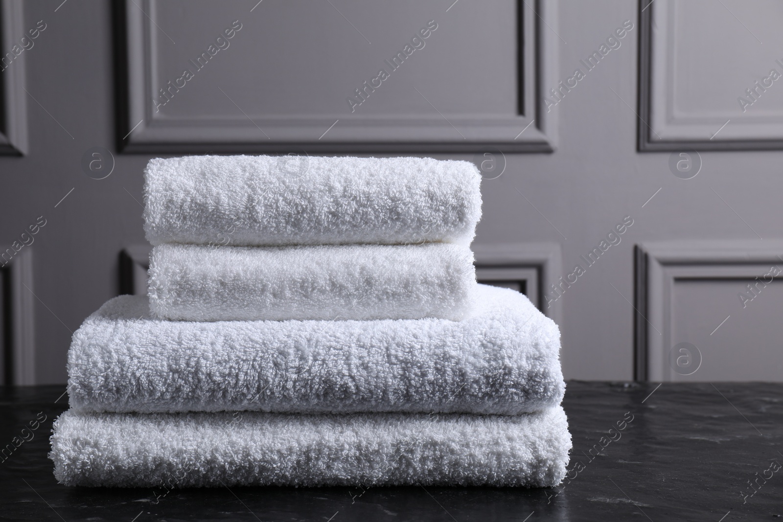 Photo of Stacked terry towels on black textured table indoors, space for text