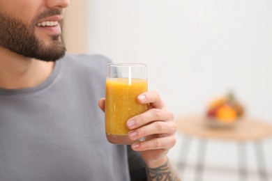 Man with delicious smoothie at home, closeup. Space for text