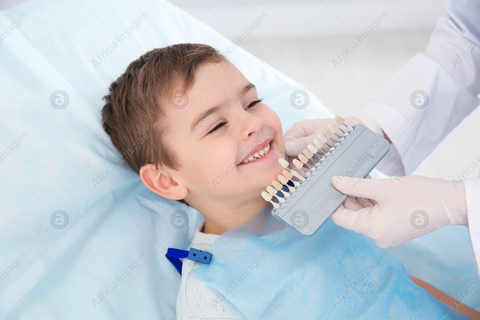 Photo of Dentist selecting cute boy's teeth color with palette in clinic
