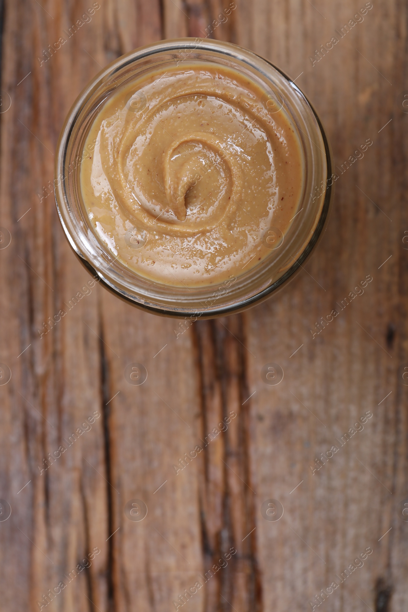 Photo of Tasty nut paste in jar on wooden table, top view. Space for text