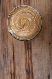 Photo of Tasty nut paste in jar on wooden table, top view. Space for text