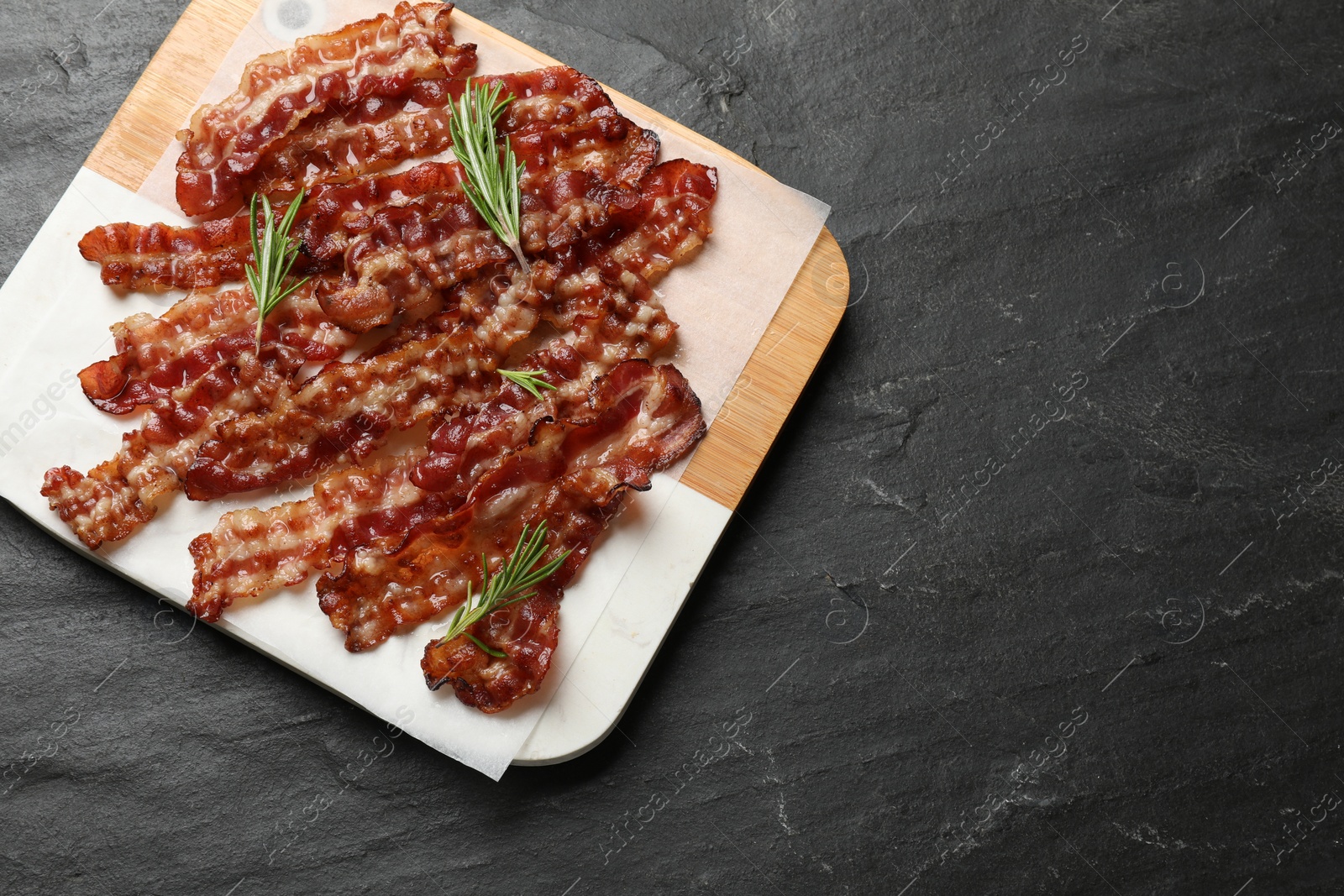 Photo of Slices of tasty fried bacon and rosemary on black table, top view. Space for text