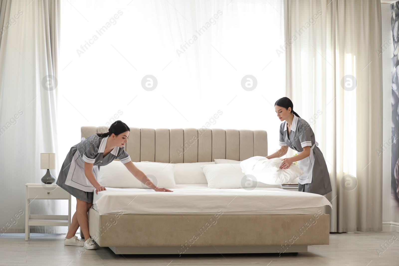 Photo of Young chambermaids making bed in hotel room