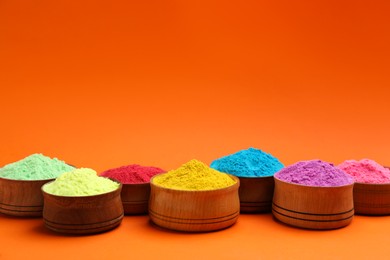 Photo of Colorful powders in wooden bowls on orange background, space for text. Holi festival celebration