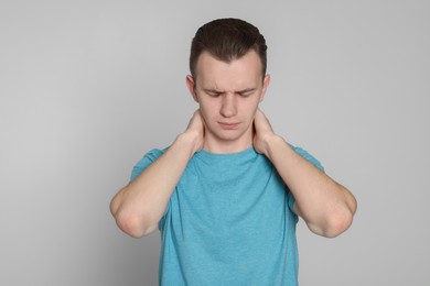 Photo of Young man suffering from neck pain on light grey background. Arthritis symptoms