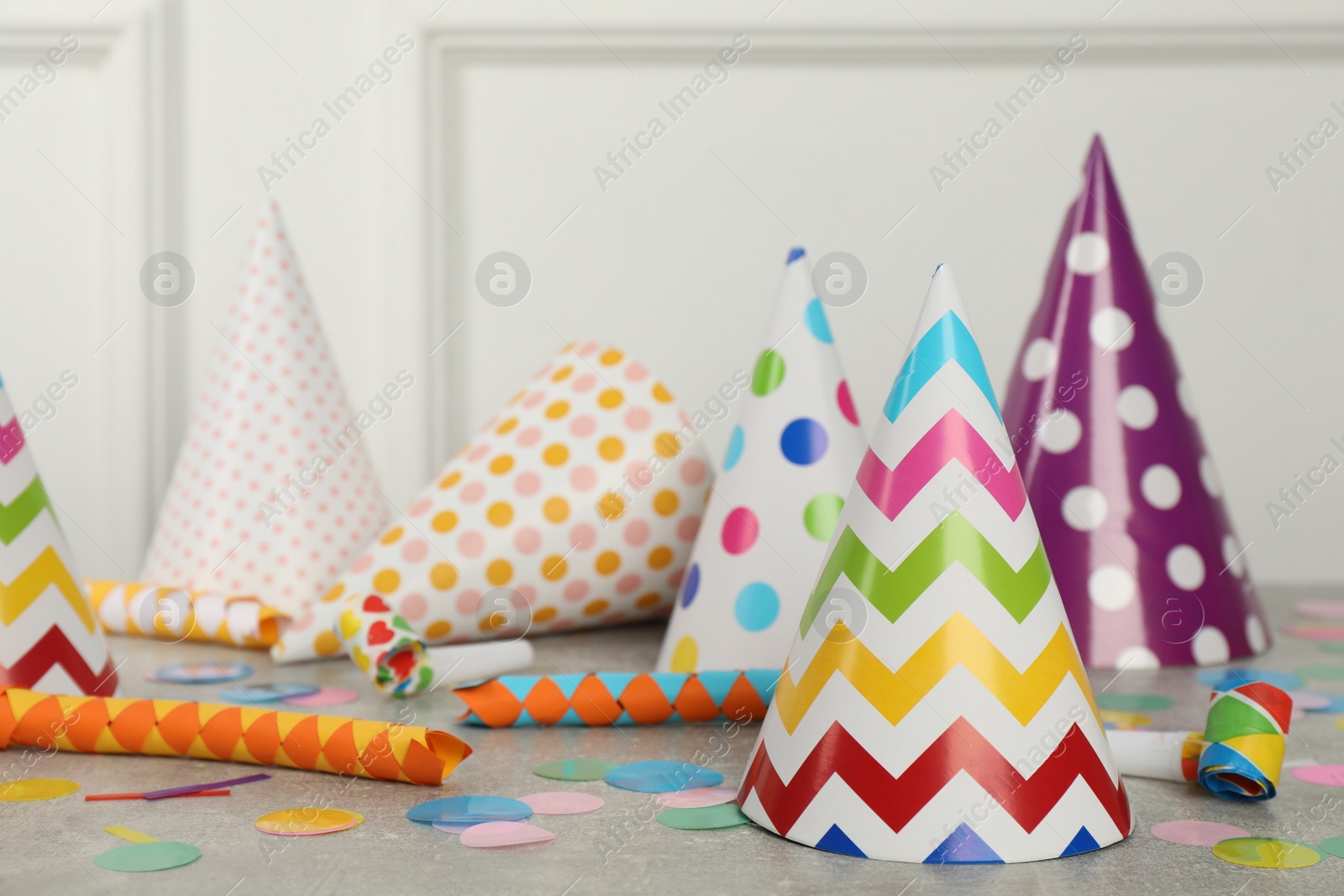 Photo of Colorful party hats and festive items on grey table near white wall indoors