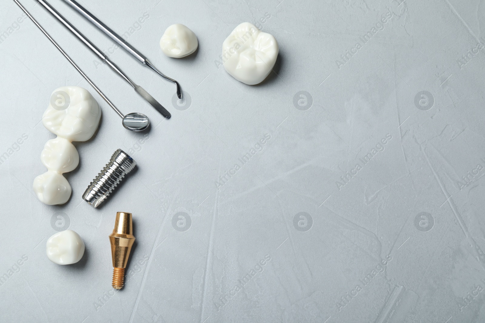 Photo of Post, abutment and different crowns of dental implant near medical tools on grey background, flat lay. Space for text