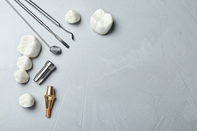 Post, abutment and different crowns of dental implant near medical tools on grey background, flat lay. Space for text