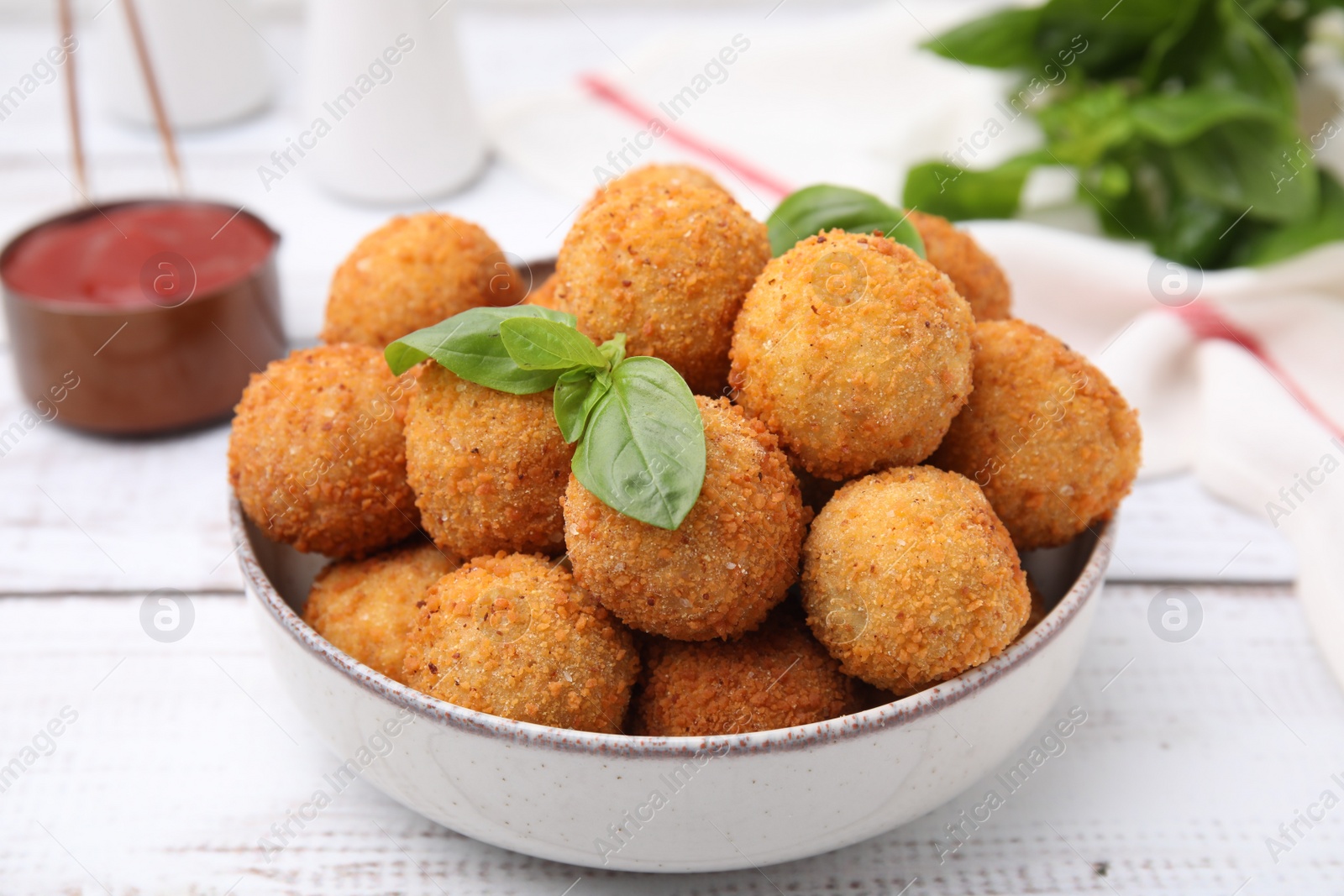 Photo of Bowl of delicious fried tofu balls with basil on white wooden table