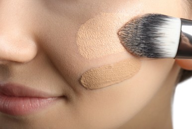 Photo of Girl applying foundation and concealer with brush on white background, closeup. Face contouring