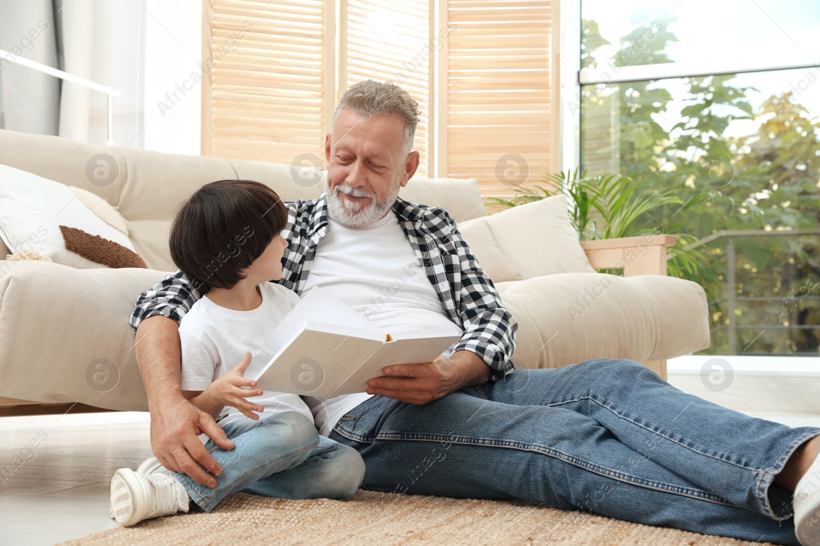 Photo of Happy grandfather with his grandson reading book together at home