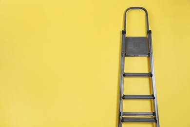 Photo of Metal stepladder on yellow background. Space for text