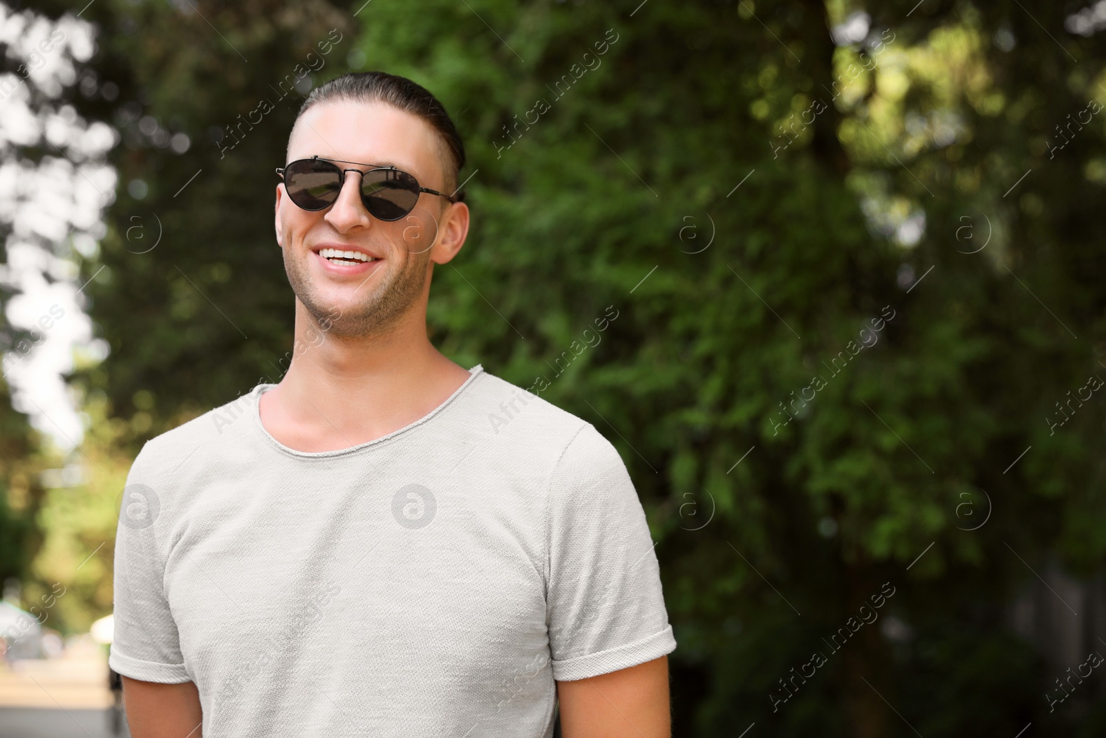 Photo of Handsome young man in stylish sunglasses at park, space for text