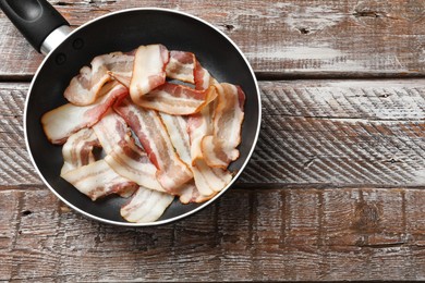 Delicious bacon slices in frying pan on wooden table, top view. Space for text