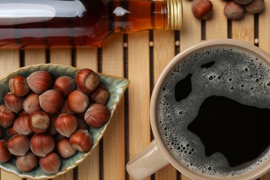 Photo of Mug of aromatic coffee, syrup and hazelnuts on wooden table, closeup