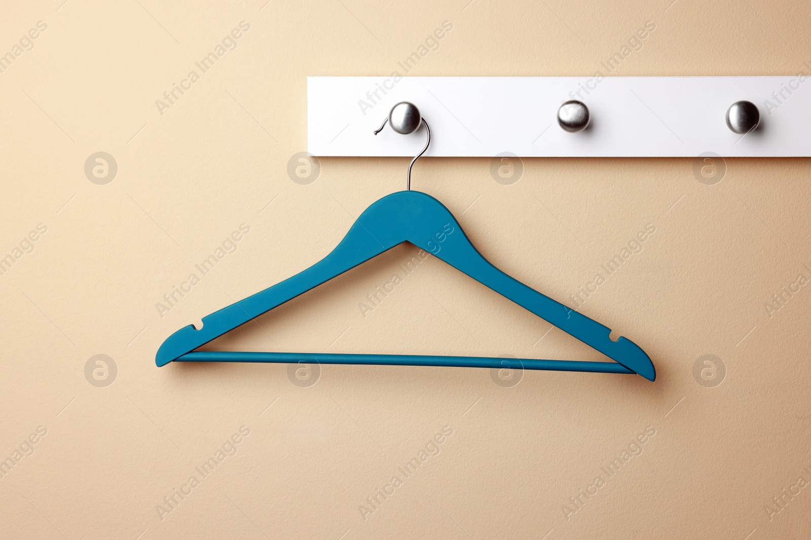 Photo of Rack with empty turquoise clothes hanger on beige wall