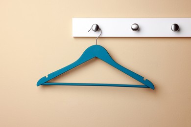 Photo of Rack with empty turquoise clothes hanger on beige wall