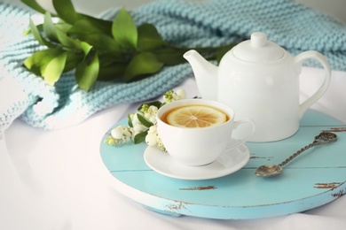 Photo of Wooden board with cup of lemon tea and teapot on fabric