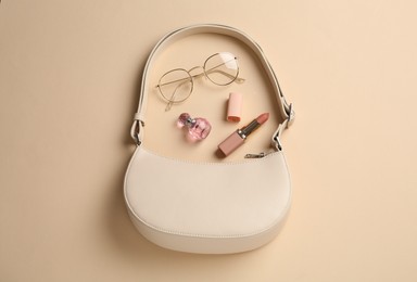 Photo of Stylish baguette bag, glasses, perfume and lipstick on beige background, flat lay