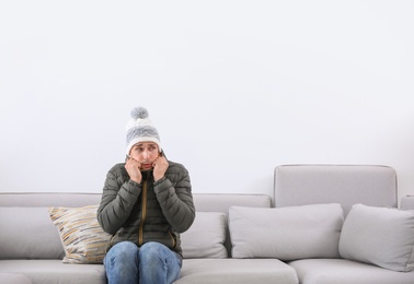 Photo of Young man wearing warm clothes freezing on sofa at home. Air conditioner malfunction