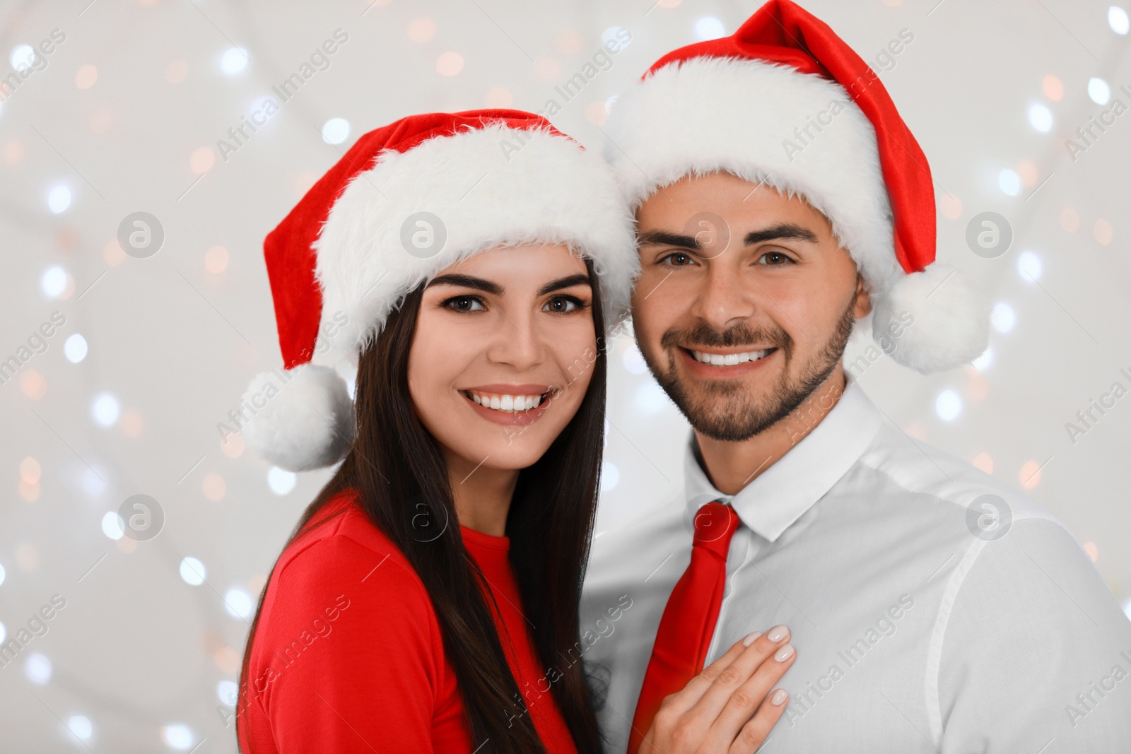 Photo of Lovely young couple in Santa hats against blurred festive lights. Christmas celebration