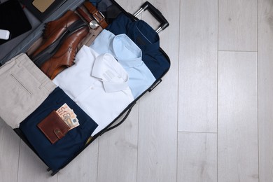 Folded clothes, shoes and accessories in open suitcase on wooden background, top view with space for text. Business trip preparations