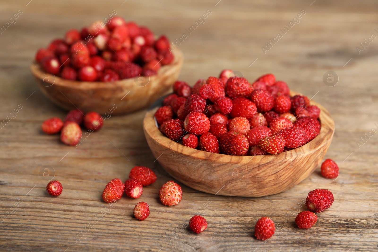 Photo of Fresh wild strawberries in bowls on wooden table